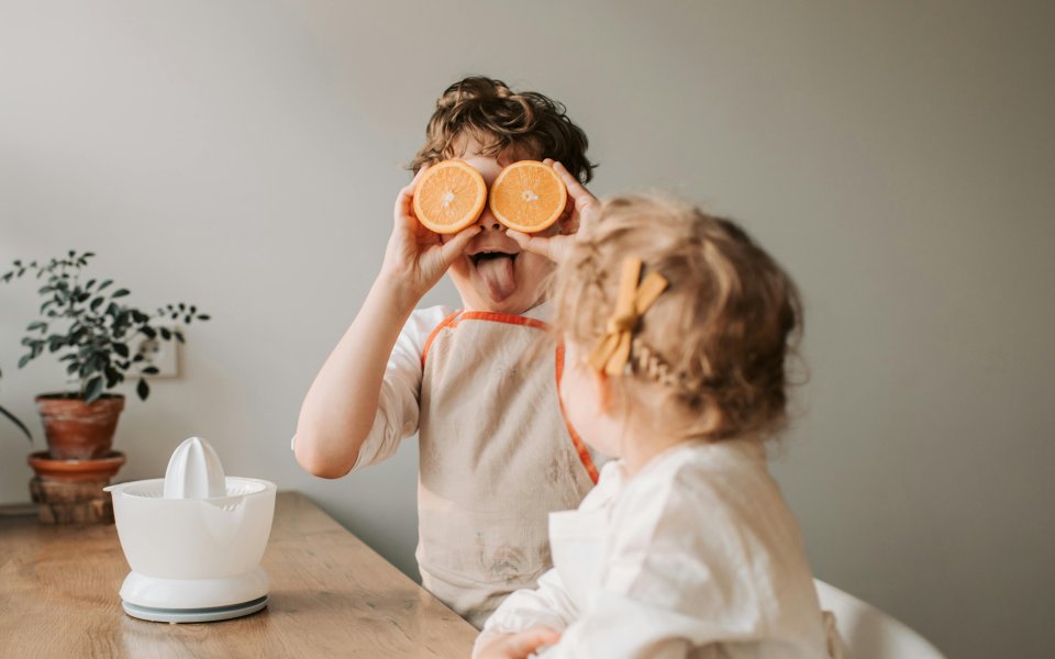 2-kinderen-aan-tafel--eentje-houdt-doorgesneden-appelsien-als-ogen-voor-gezicht