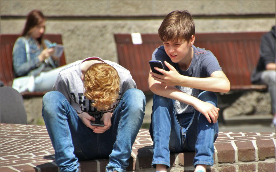 2-tieners-zitten-op-een-muurtje-en-kijken-op-hun-smartphone