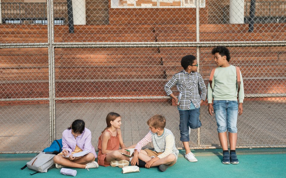 5-jonge-tieners-met-schoolgerief--zittend-en-leunend-tegen-een-hek