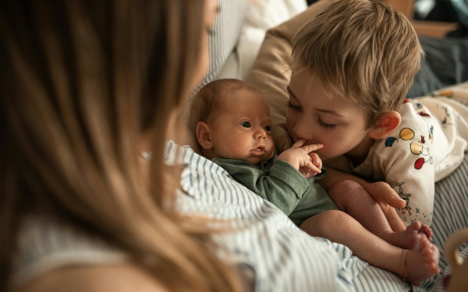 broertje-kijkt-naar-pasgeboren-baby-die-in-armen-van-mama-ligt