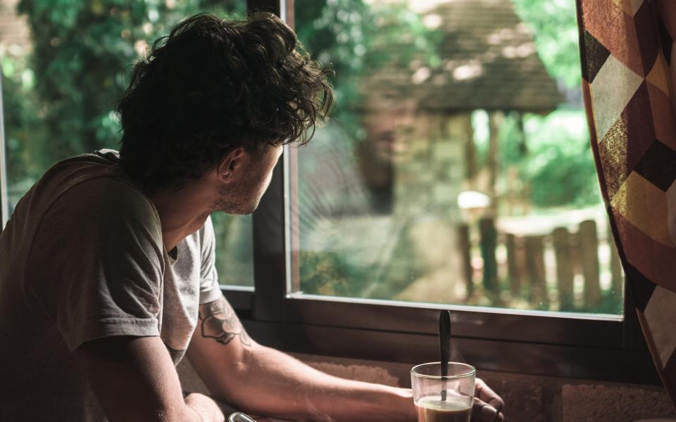 Een man drinkt koffie en kijkt uit het raam