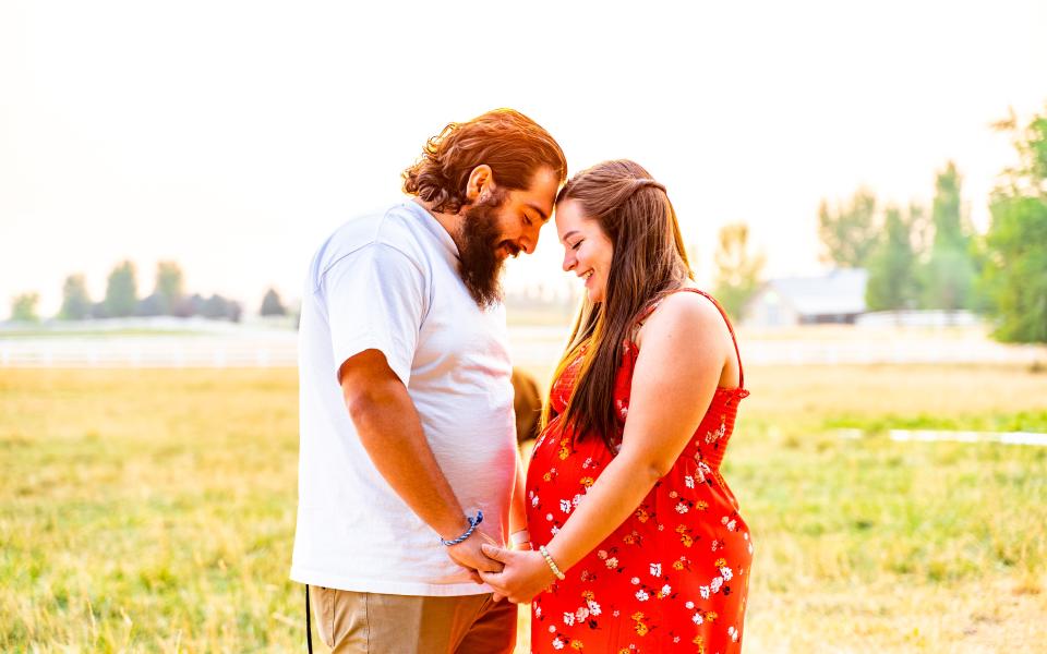 Een vader staat met zijn zwangere vrouw in een veld