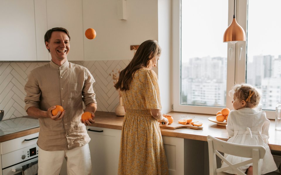 gezin-in-keuken--peuter-helpt--vader-jongleert-met-appelsienen