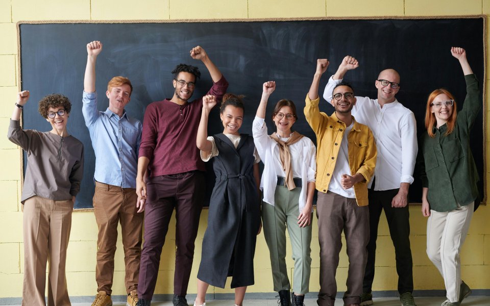 leerkrachten-op-een-rijtje-voor-een-schoolbord--juichend