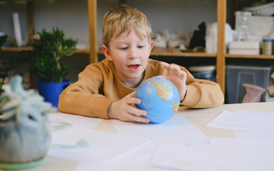 leerling-zit-aan-tafel-met-wereldbolletje-in-zijn-handen