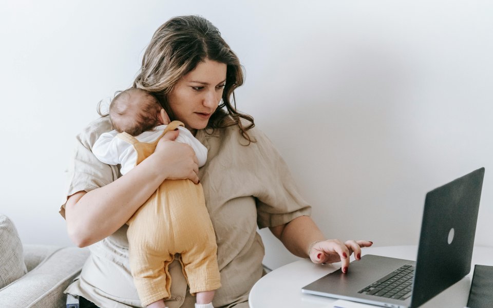 jonge mama die baby vasthoudt terwijl ze op laptop werkt