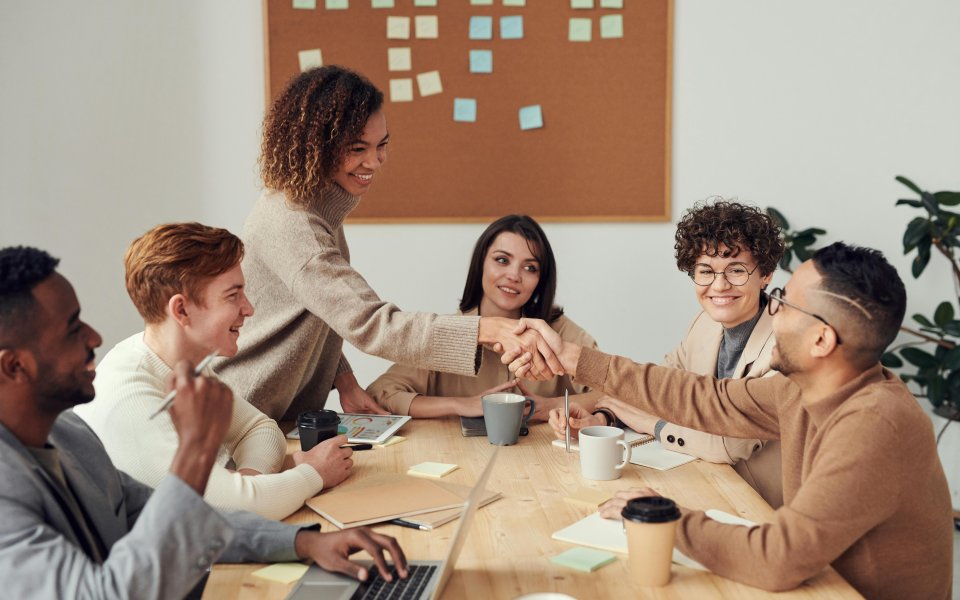 tafel-met-mensen-die-overleggen--1-vrouw-schudt-iemand-de-hand