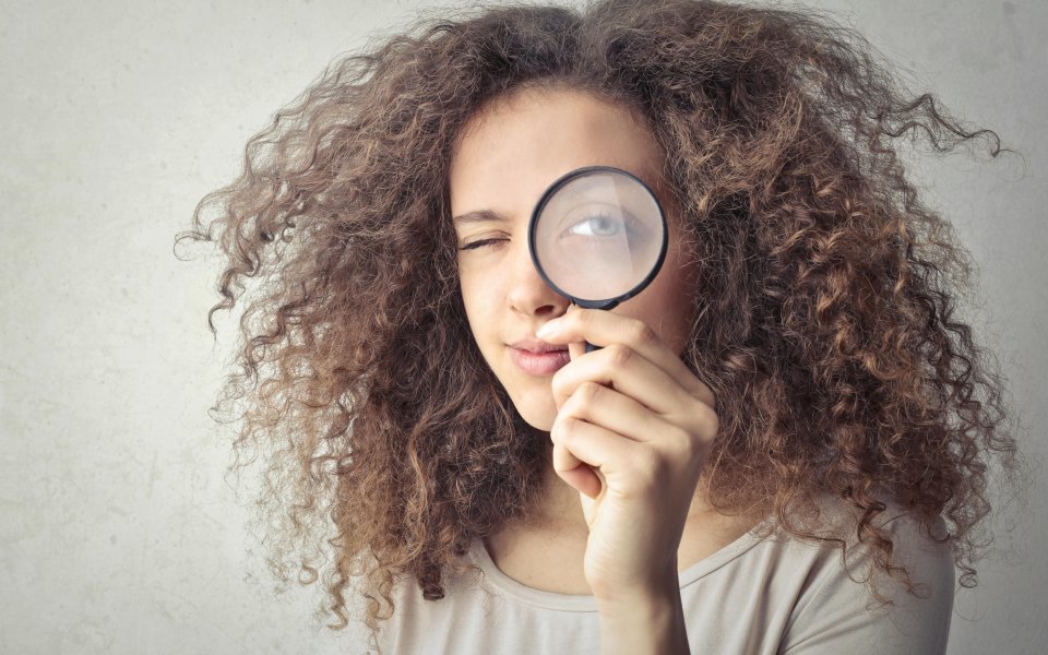 jonge vrouw kijkt door vergrootglas met 1 oog