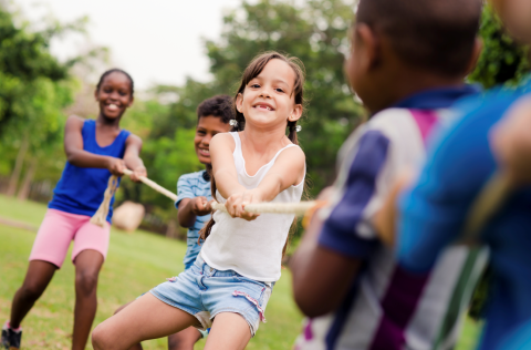 Een diverse groep kinderen speelt buiten touwtrekken